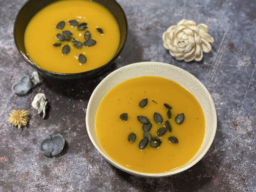 A bowl of creamy pumpkin soup garnished with pumpkin seeds served in a futuristic modern setting.
