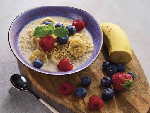 A bowl of banana-bulgur porridge topped with fresh fruit, served in a white dish on a wooden table.