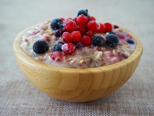 A bowl of oatmeal topped with fresh fruits such as strawberries, bananas, and blueberries, served with a plant-based drink.