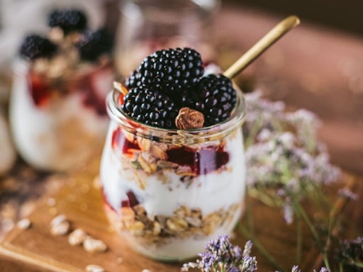 A glass jar filled with oatmeal topped with fresh strawberries, blueberries, and a drizzle of honey, set on a wooden surface.
