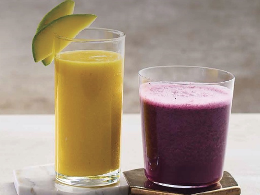 An orange smoothie made from oranges and a red smoothie made from beetroot, both in glass jars, surrounded by fresh ingredients, placed on a plate.